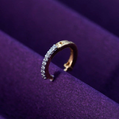 A gold and diamond nose ring on a purple cushion.