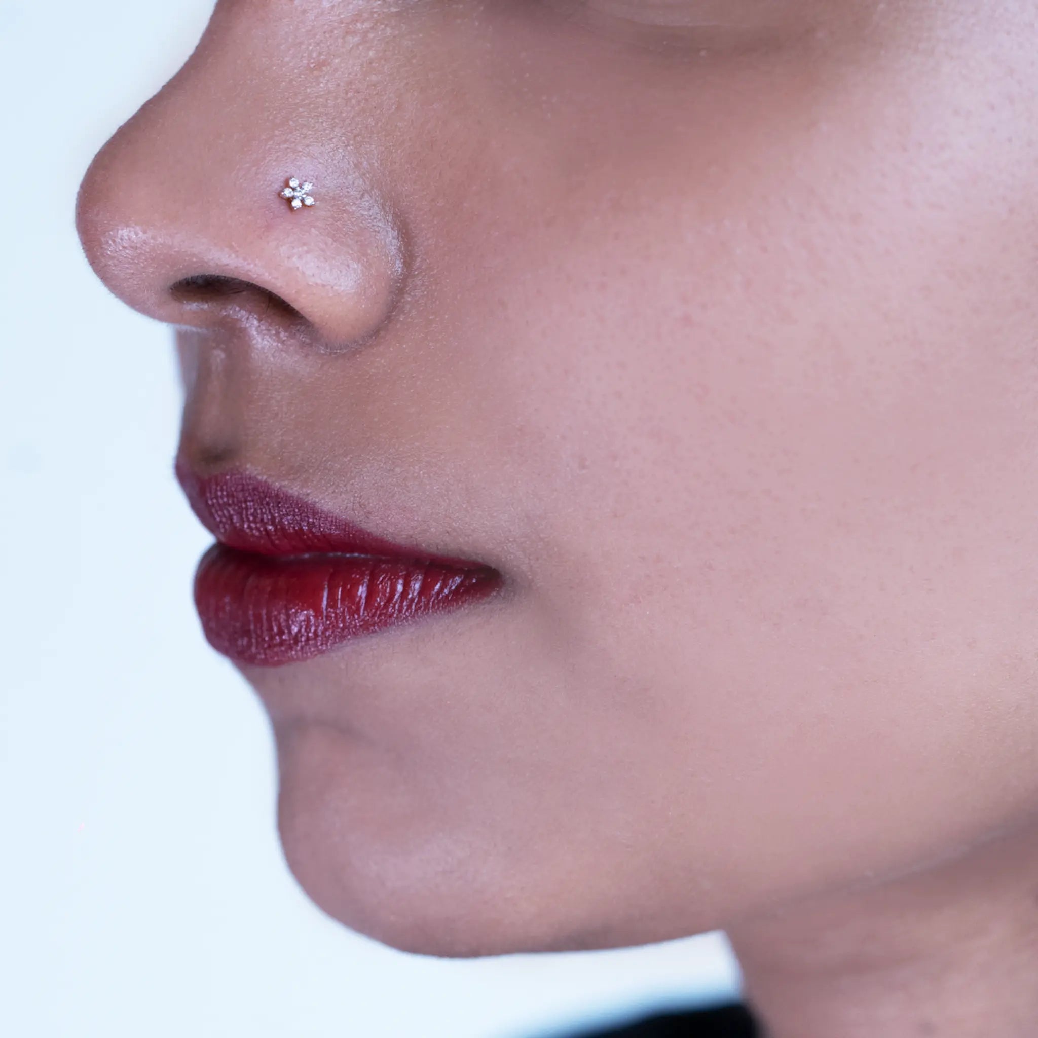 Model wearing a six-stone flower shaped diamond nose pin in 18k gold on her left nostril, showing the fit and scale of the diamond nose pin setting against skin.