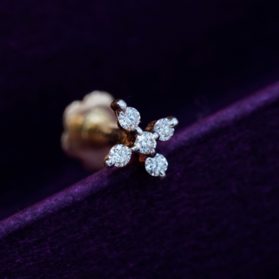 A gold nose pin with five diamond stones arranged in a floral pattern, displayed against a purple background.